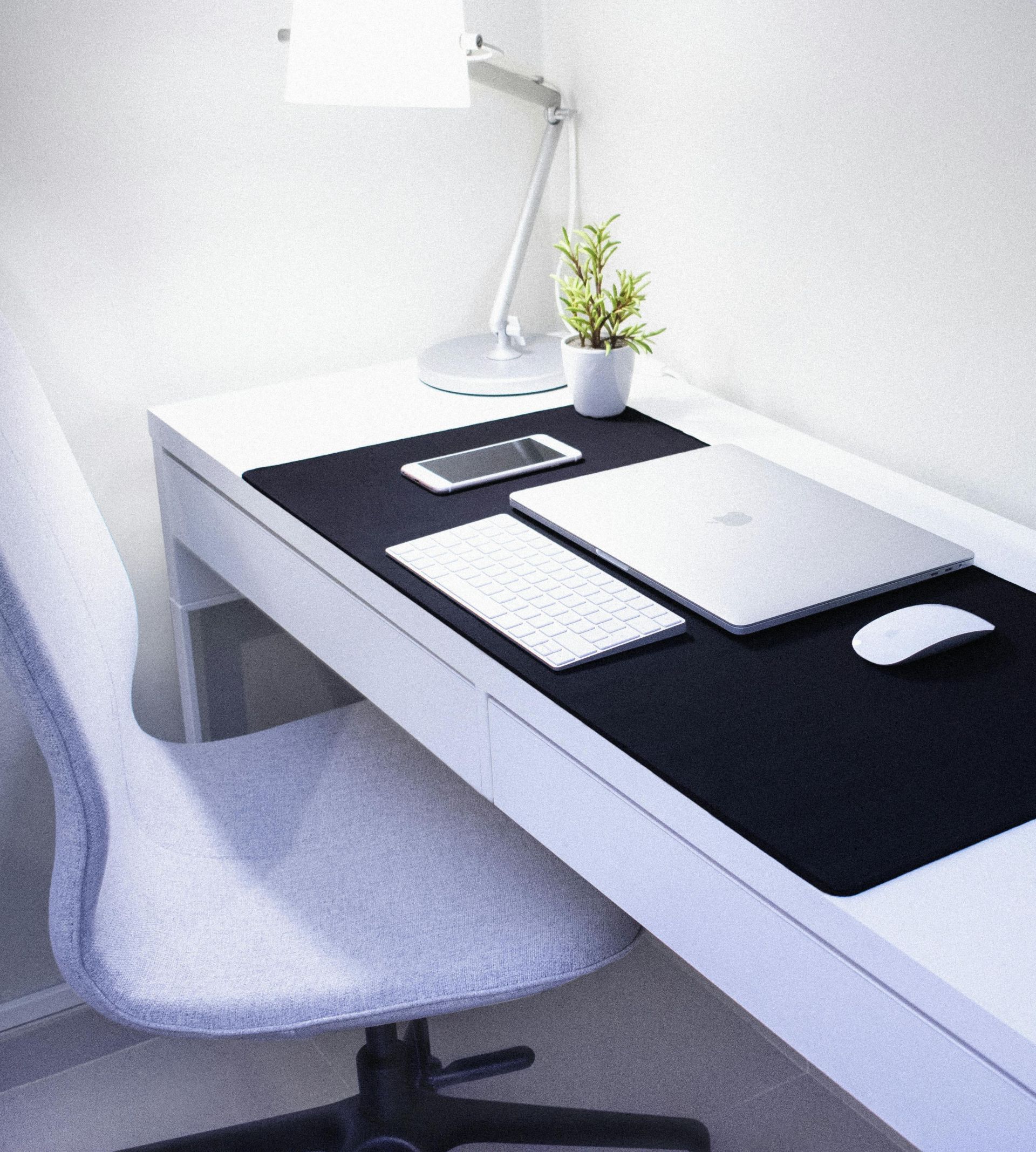 Sleek, modern home office setup featuring Apple devices, a desk lamp, and a plant.